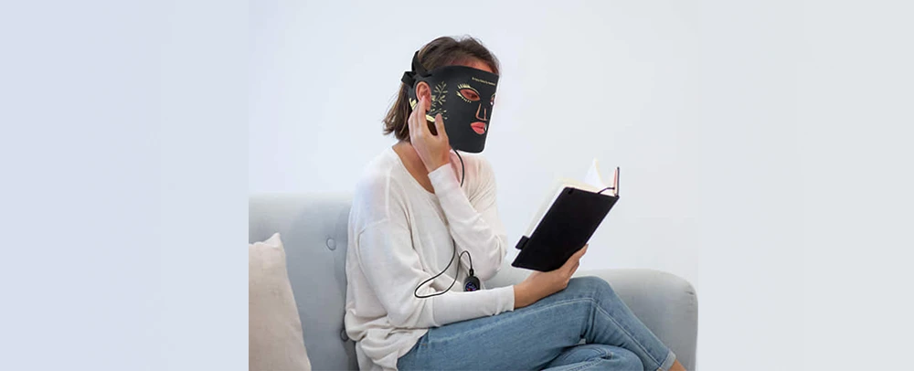 a women wearing red ligh therapy maks and reading book